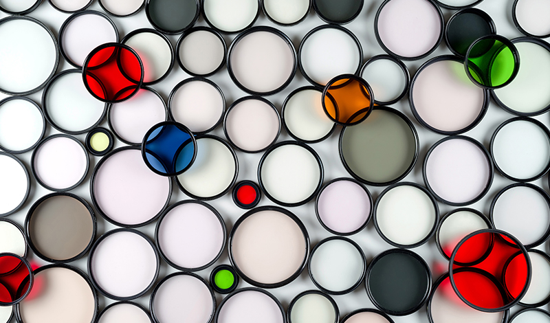 Multicolored round glass photographic filters of various sizes on a light background