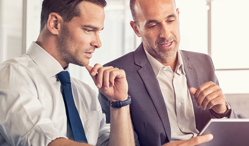 Two businessmen talking while looking at a tablet